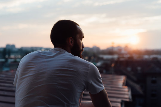 Bearded man standing on the balcony watching sunset