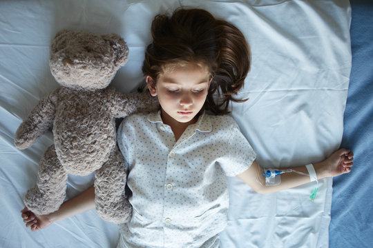 Patient child and teddy bear lying togehter on hospital bed