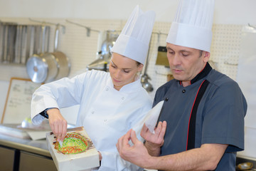 pastry chef and assistant in the kitchen decorating a cake