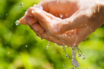 Fototapeta premium Woman washing hand outdoors. Natural drinking water in the palm. Hands with water splash, selective focus. Summer time