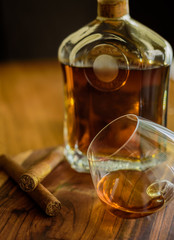 Close up of two cigars, a glass and a bottle of rum on a wooden surface