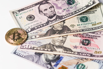 Gold bitcoin on the background of four different banknotes of US dollars.