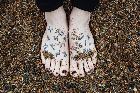 Transgender persons feet with painted nails and runes tattoos