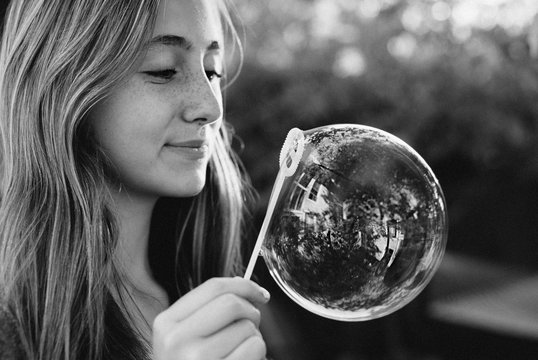 Teenage girl smiling at a bubble with a reflection of her house