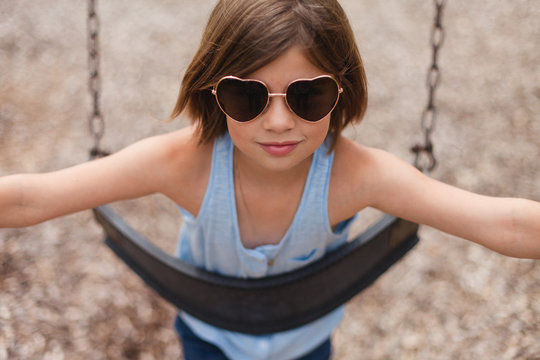 Happy girl wearing heart shaped sunglasses on a swing