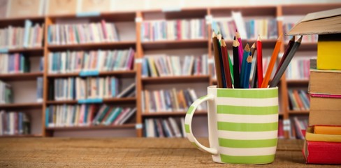 Composite image of stack of books by mug with colored pencils on