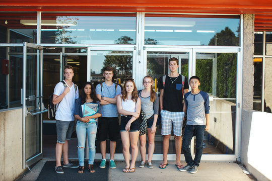 Group of serious high school teens standing in front of school on summer day