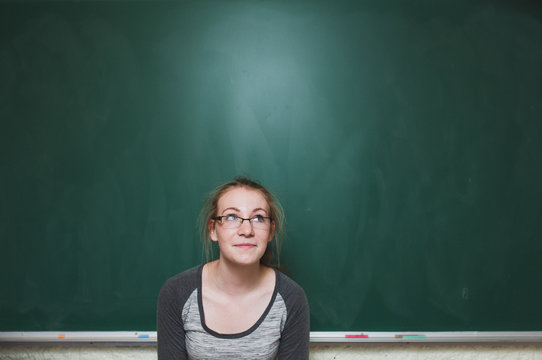 High school student standing in front of green chalkboard thinking and smiling