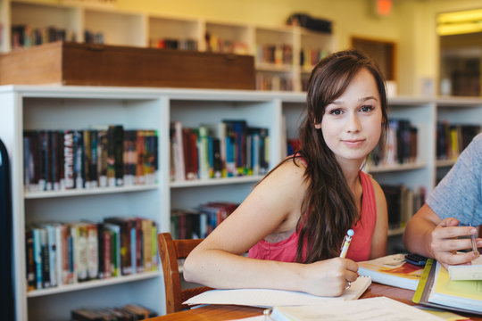 Portrait of studious high school teenage student working and writing in library