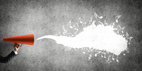 Hand of businesswoman holding red paper trumpet against concrete background