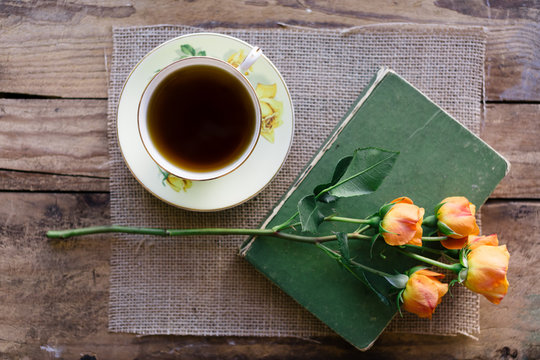 Black tea in china teacup on a hessian and wood background, with fresh orange roses