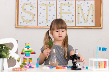 Obraz na płótnie Canvas Little girl is behind the desk. Microscope, the tree, little robot and books are near her. The word STEM is on the background. E-learning. Stem education. Cute child.