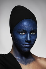 portrait of young beautiful girl. face painted with blue paint and glitter.