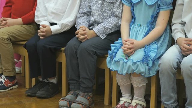 Unknown little children preschoolers in casual clothes sit on stools and posing for photographer in kindergarten in the classroom