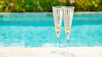 Two glasses of prosecco cocktail with orange berry at the edge of a resort pool. Concept of luxury vacation
