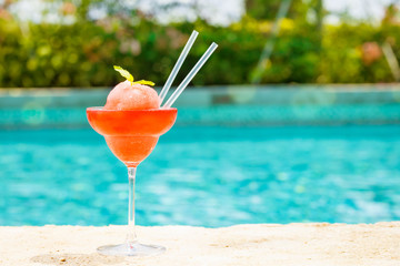 Frozen strawberry margarita cocktail at the edge of a resort pool.  Concept of luxury vacation