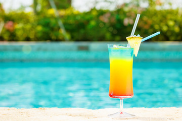 Rainbow cocktail at the edge of a resort pool.  Concept of luxury vacation
