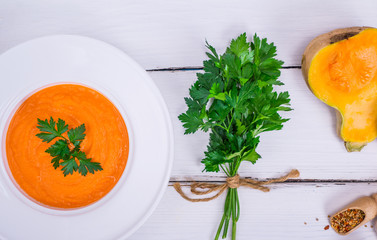 creamy pumpkin soup in a round white plate and a bunch of green parsley