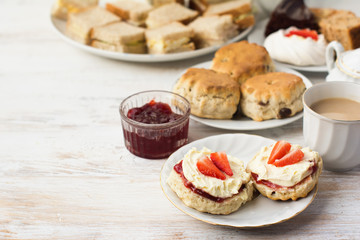English cream teas, scones with jam and cream, tea with milk, with sandwiches on the back, on the white wooden table, selective focus copy space for text