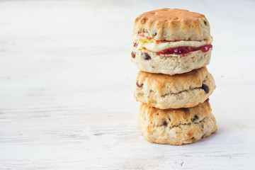 Three scones in a stack with jam and cream, on the plate, on the white wooden table, selective focus copy space for text