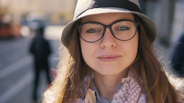 Close-up portrait of caucasian girl in a grey striped hat standing in the street, slowmotion