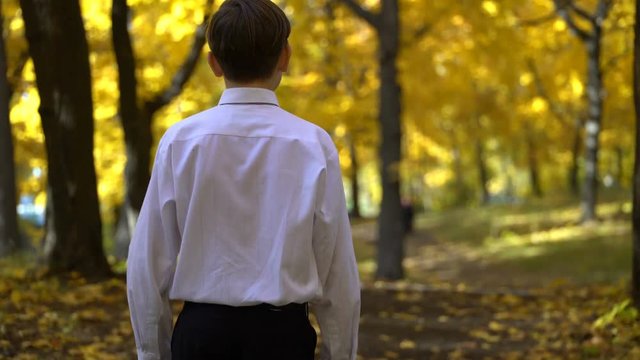 young guy in a white shirtwalks in the autumn park