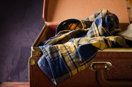 Old vintage, retro open suitcase with man's checkered shirt on dark background. Travel concept