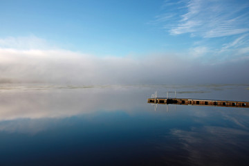 Fototapeta premium Sky and dock reflection at lake in foggy morning