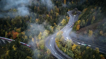 Poster Im Rahmen street from above trough a misty forest at autumn, aerial view flying through the clouds with fog and trees © visualitte