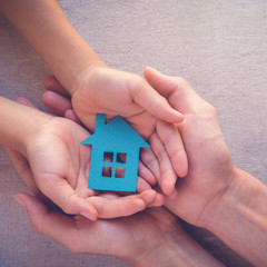 Adult and child hands holding paper house, family home and real estate concept