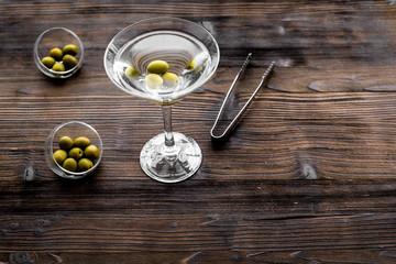 Make martini cocktails. Glass with beverage, olives and utensils on dark wooden background top view copyspace