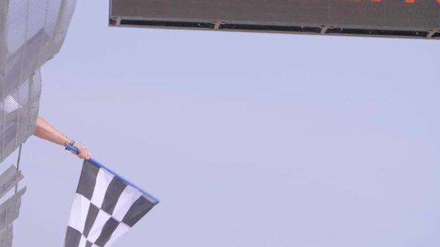 Man holding and waving Checkered race flag in slow motion at finish line on a raceway. Victory, achievement, success and sport concept.