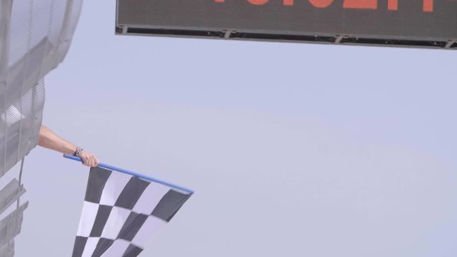 Man holding and waving Checkered race flag in slow motion at finish line on a raceway. Victory, achievement, success and sport concept.