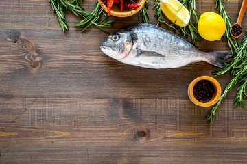 Mediterranian cuisine. Dorado with rosemary, pepper, chili, lemon on wooden background top view copyspace