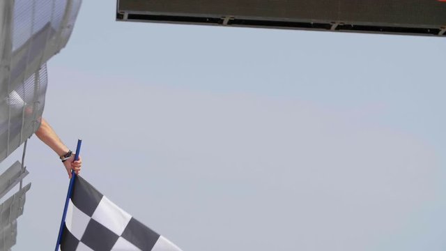 Man holding and waving Checkered race flag in slow motion at finish line on a raceway. Victory, achievement, success and sport concept.