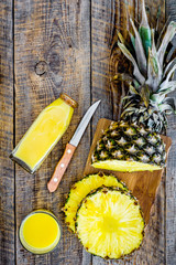 Preparing pineapple juice. Bottle with beverage near fruit slices and knife on wooden background top view copyspace