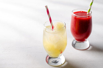 Strawberry smoothies and ice lemonade with cocktail tubes in glasses, on white background.