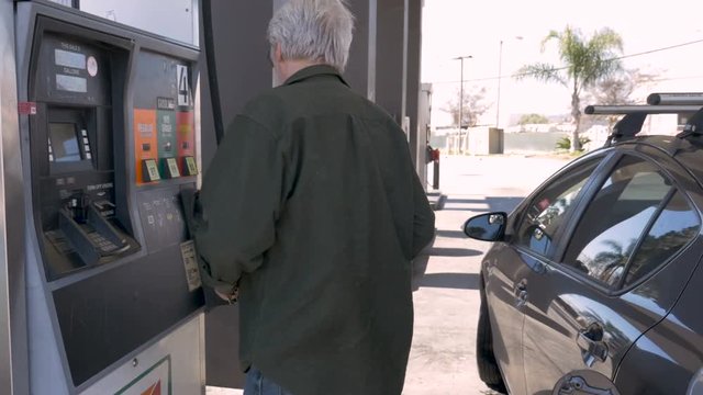 Elderly man pumping gas into his car from a self serve gas station
