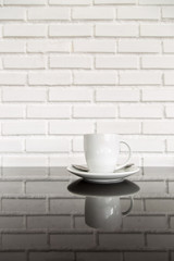 white cup of hot coffee on top of glass table with white brick wall background. concept fot drink and food