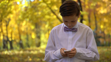 young guy playing in the phone and walking in the autumn park.
