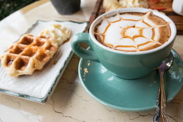 Cappuccino in green glass and waffles with vanilla ice cream.