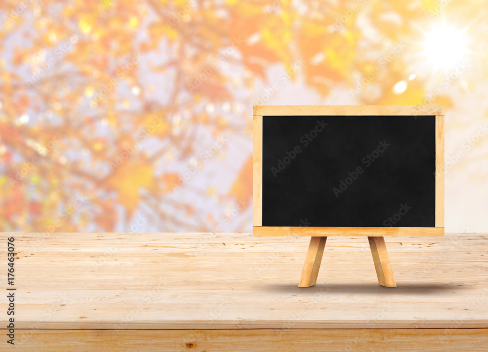 Poster blackboard with easel on wood table top with blur maple leaf with sunlight,autumn backgorund,mock up