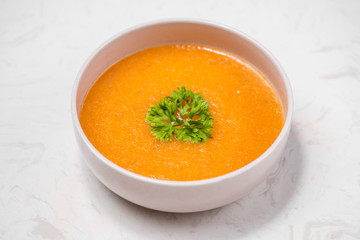 Carrot soup with cream and parsley on white stone background. Top view. Copy space