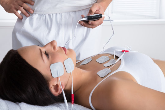 Therapist Giving Electrodes Therapy On Woman's Chest And Face