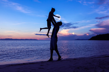Silhouette father and daughter on the beach with the moon and blue sky