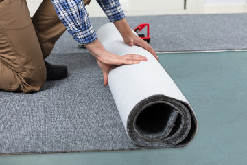 Male Handyman Rolling Carpet On Floor