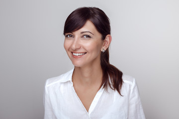 Closeup portrait of beautiful smiling young middle age brunette Caucasian woman with brown eyes looking in camera. Girl female with long dark hair in white office shirt. Studio beauty shot. - obrazy, fototapety, plakaty