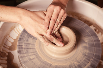 Close-up of a woman beautifully sculpts from a brown clay a deep plate on a potter's wheel, a top view