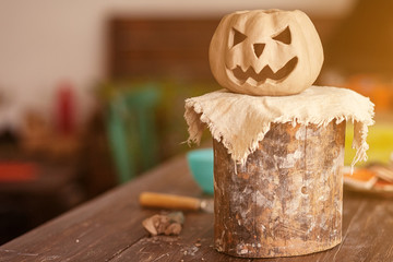 A small clay pumpkin with jack's face for halloween stands on a wooden stand on a wooden table in a beautiful workshop