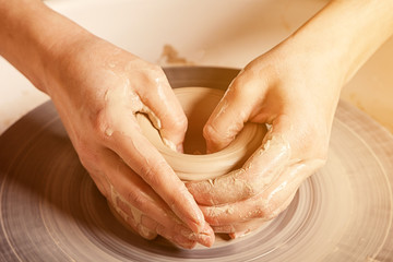 Close-up of a young woman potter beautifully sculpts a brown clay vase and makes for her neck on a potter's wheel, a top view